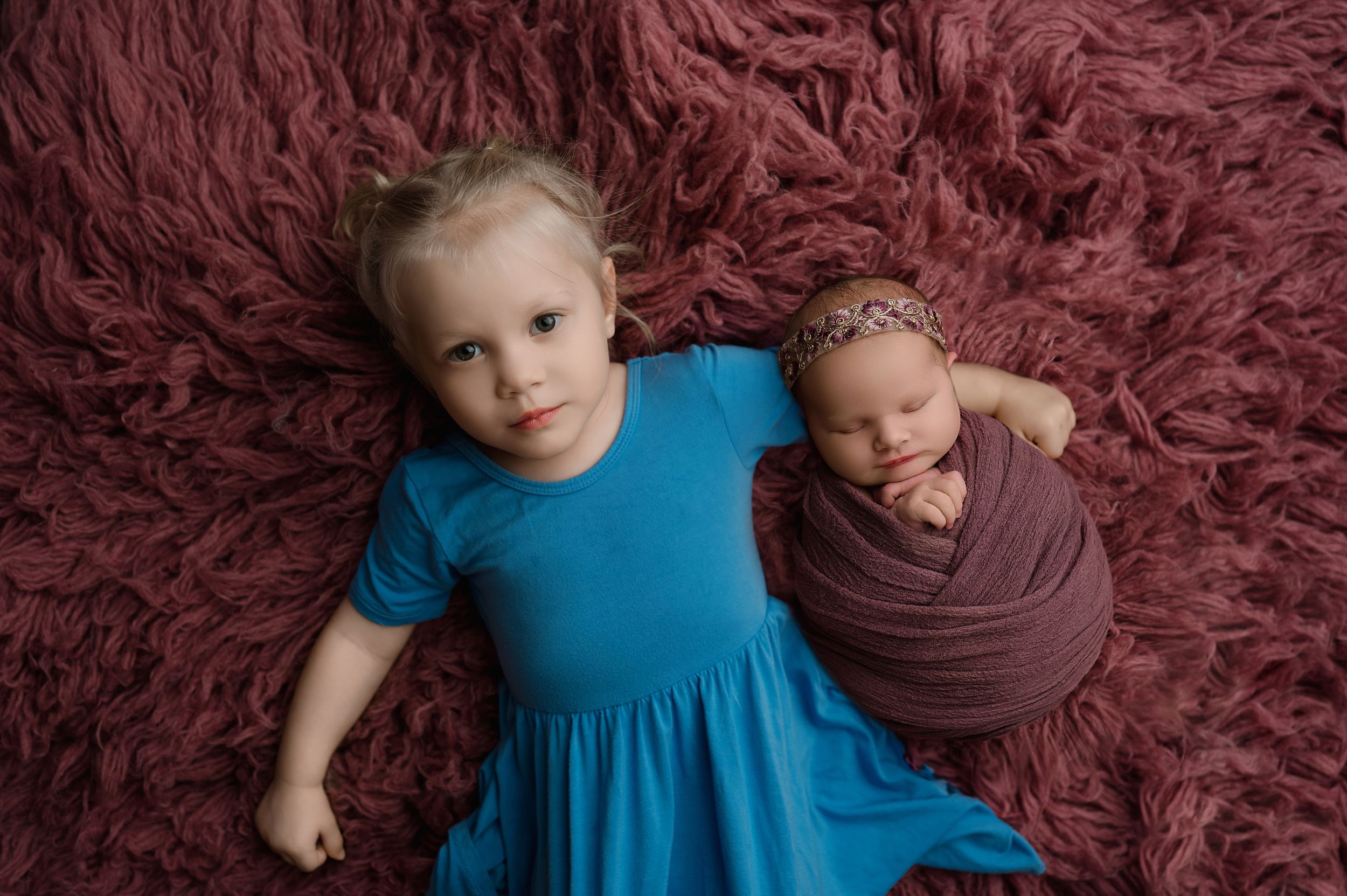Two children in coordinating blue and brown outfits pose together on a burgundy textured backdrop.