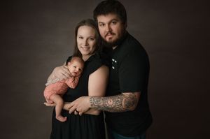 Professional studio portrait with moody brown backdrop showcasing tattoo art and family embrace.