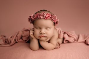 Sweet sleeping infant in pink tones wearing delicate flower crown in artistic newborn photo session.