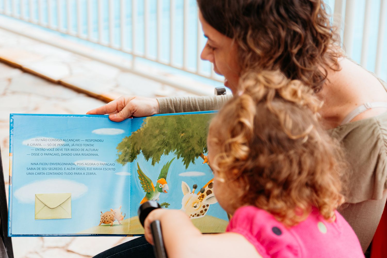 A young child and adult read a picture book together while sitting in a cozy chair.