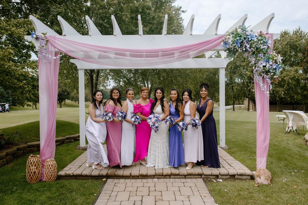 Outdoor wedding party photos with bridesmaids in colorful dresses posing under pink fabric draped archways.