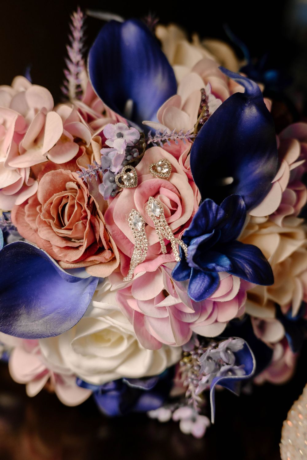 Close-up of delicate pink roses and deep blue flowers arranged with sparkling crystal accents.