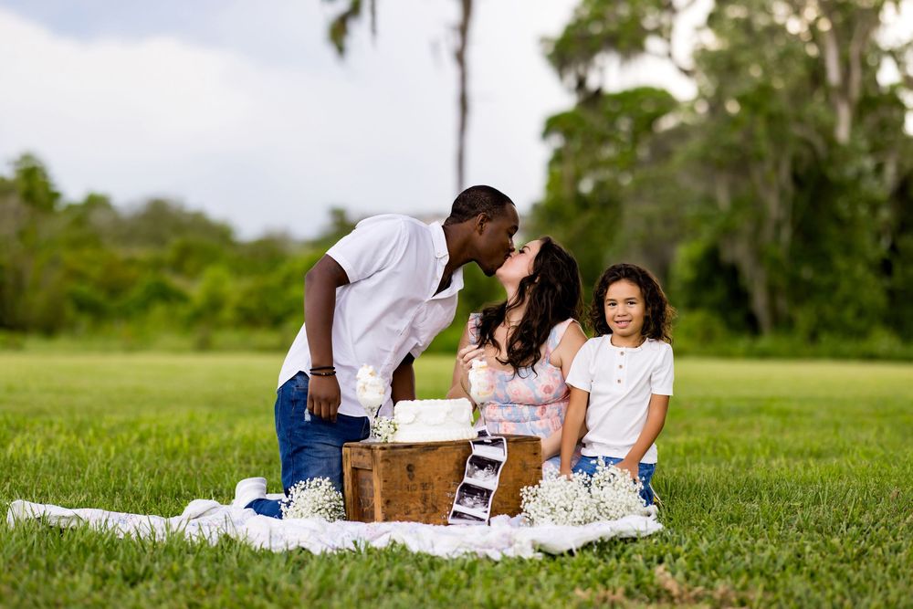 Family enjoying a relaxing outdoor picnic together on a white blanket in a lush green field.