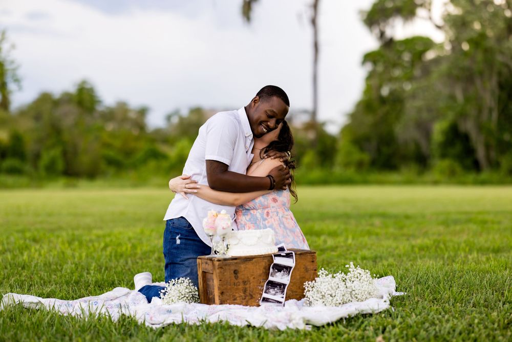 A person sits on a white blanket in a lush green field while reading a book or document on a sunny day.