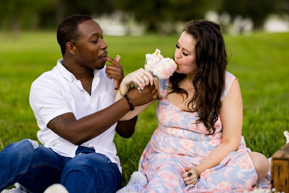 A couple enjoys a picnic on a grassy lawn on a sunny day, sharing food while sitting together on a blanket.