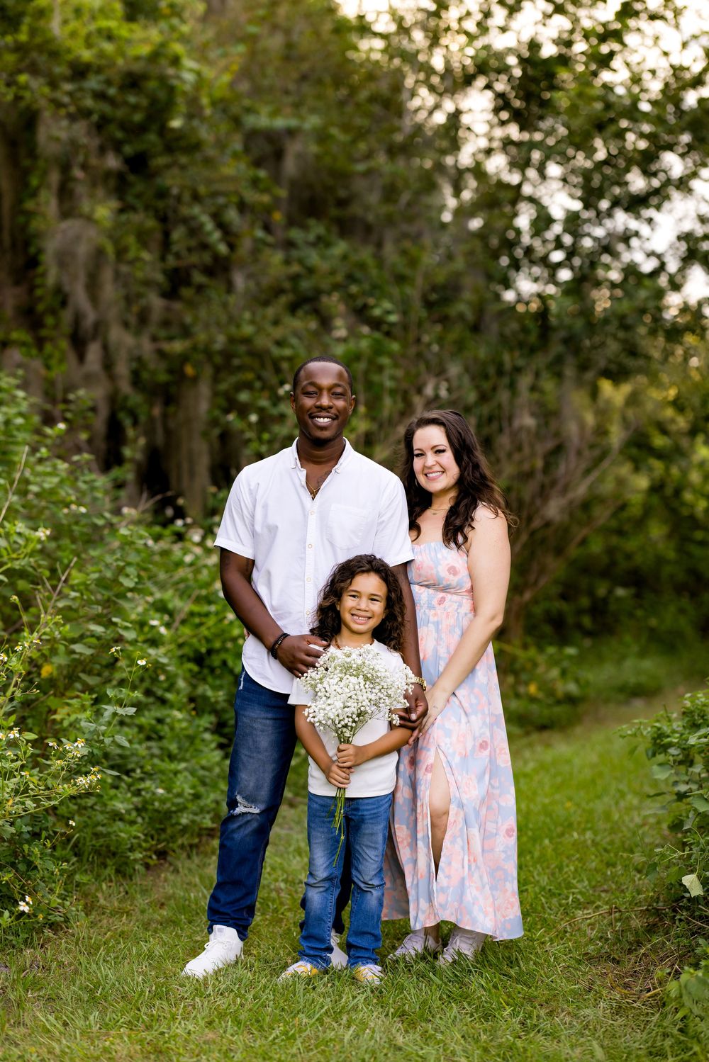 A happy family enjoying a casual outdoor photo session in a lush green natural setting at sunset.