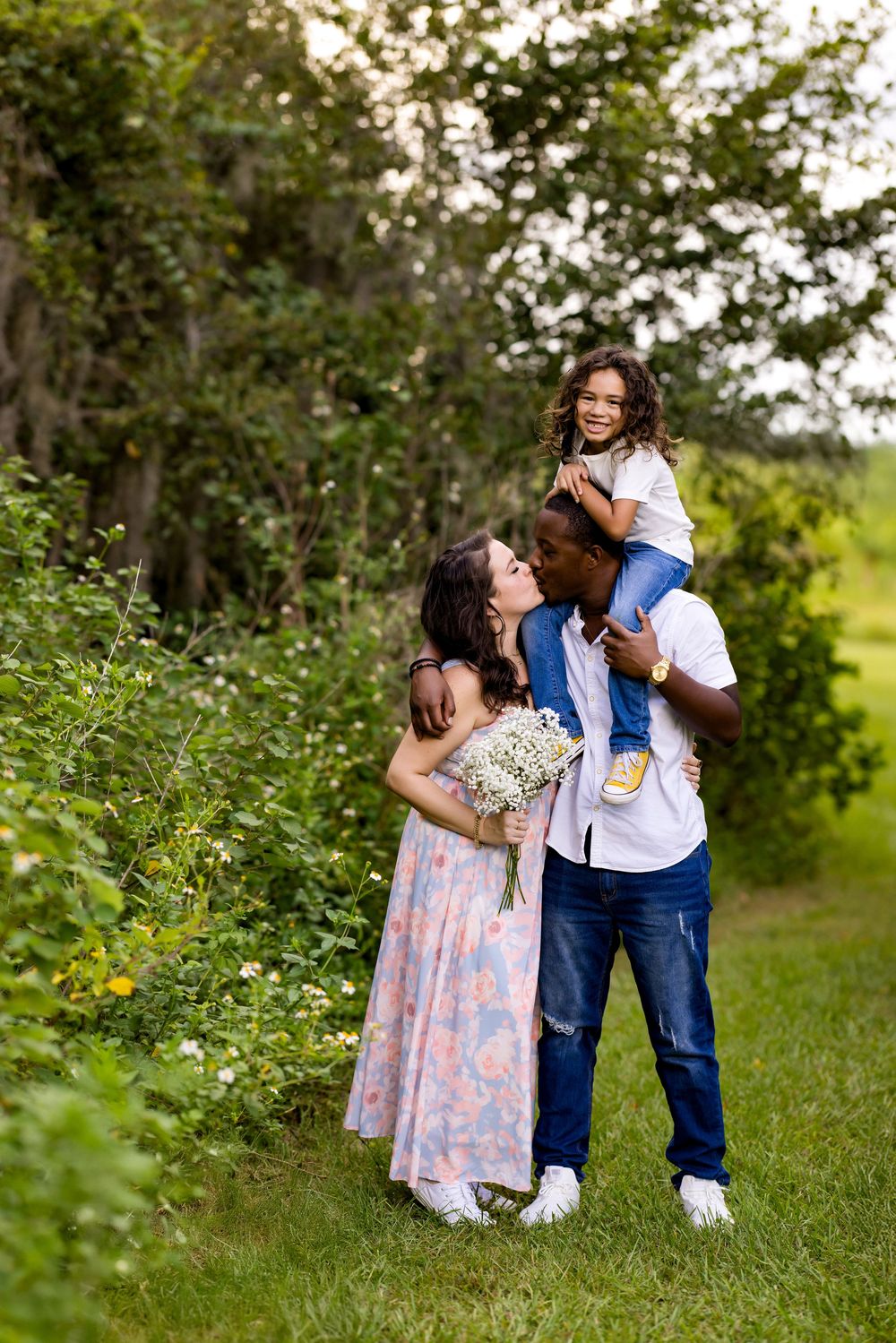 A family shares a tender moment together on a nature path with flowers and greenery in the background.