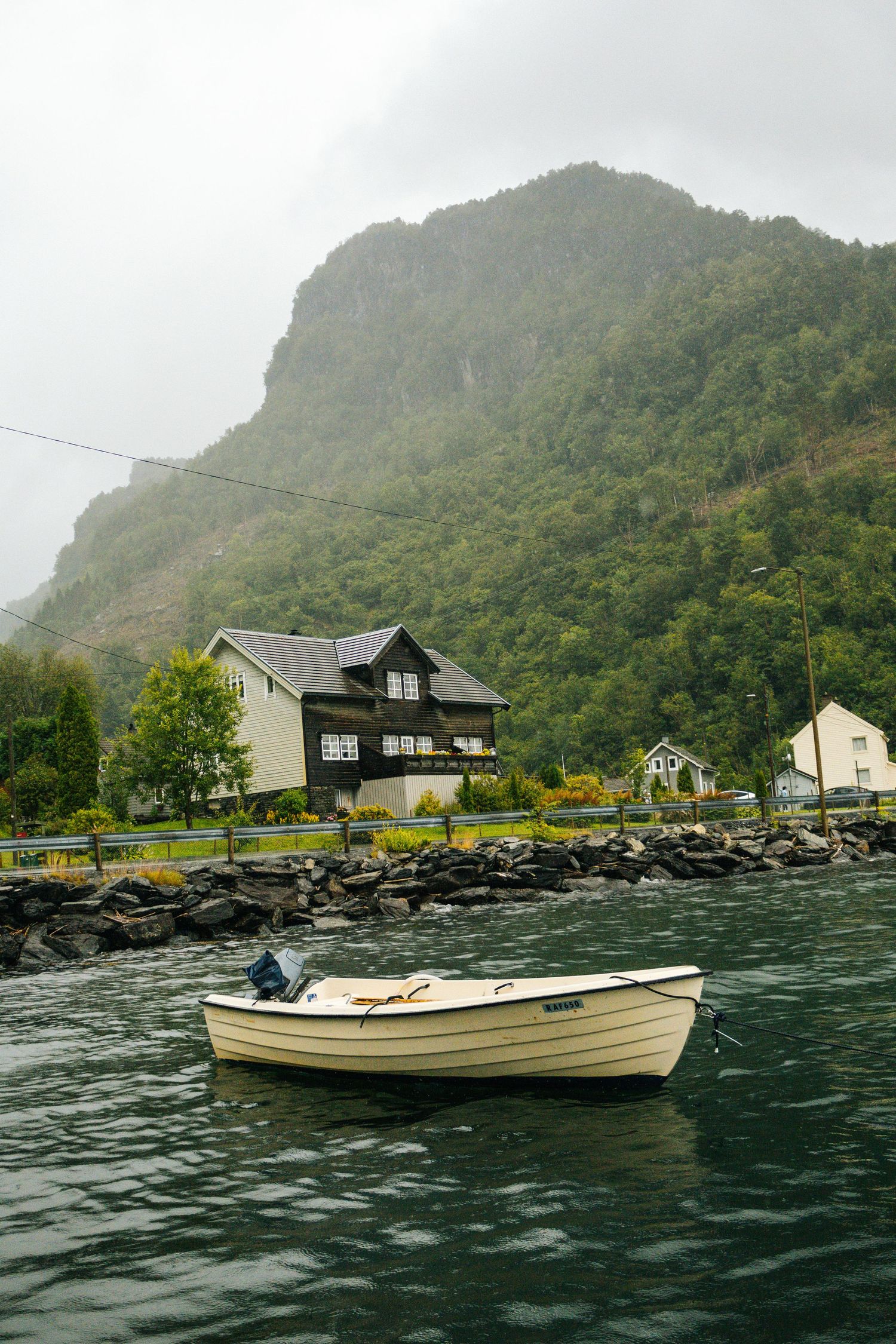 Scenic coastal landscape with boats and houses along rocky shoreline beneath green mountains.