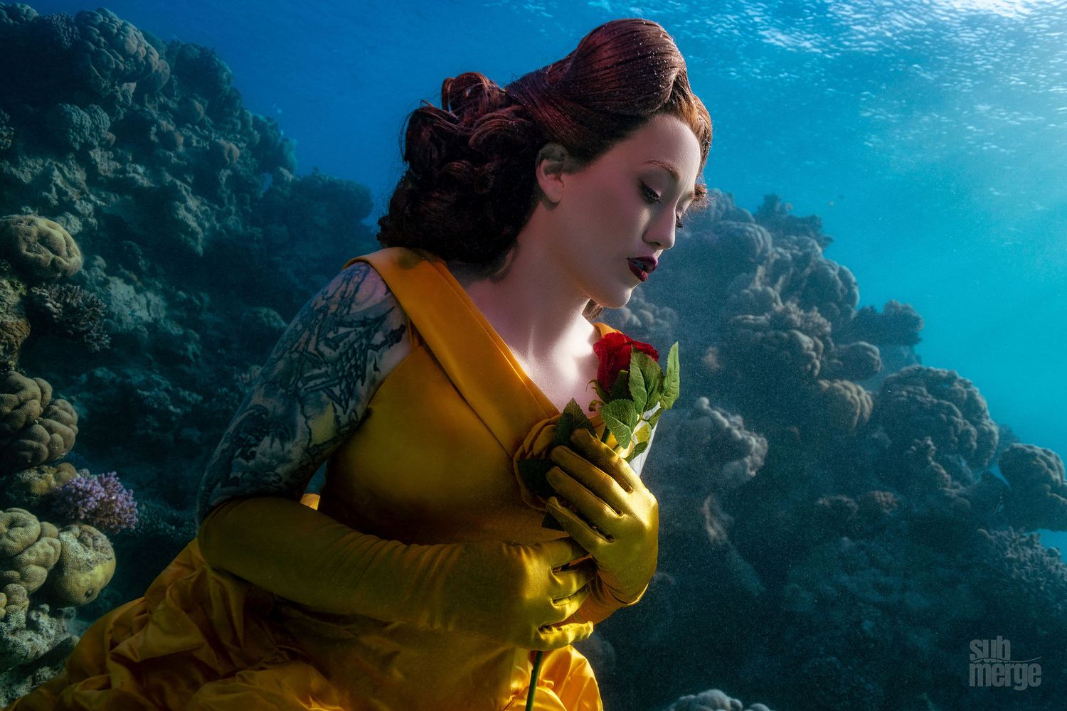 A person in a yellow jacket diving underwater surrounded by a bright blue ocean background.