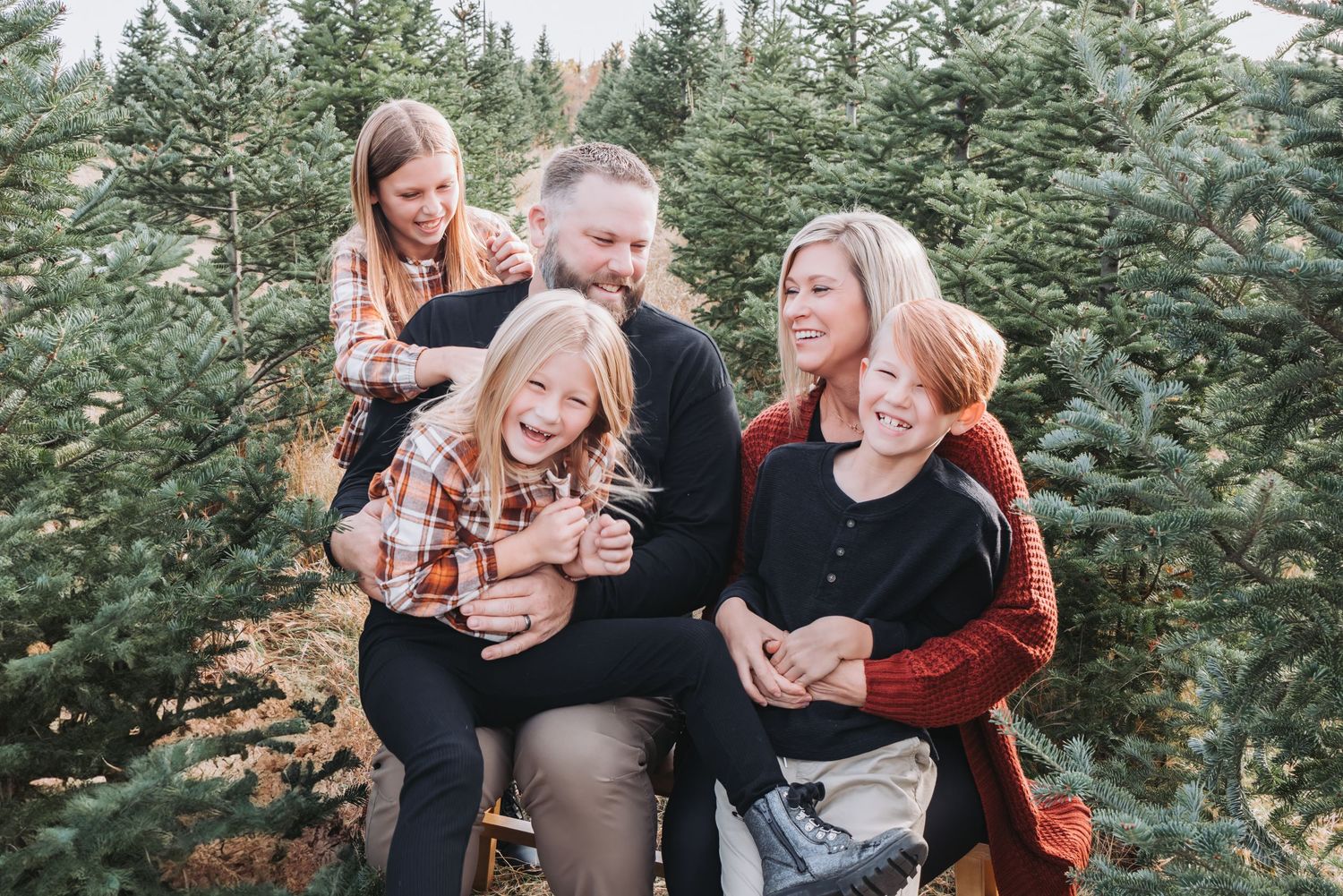 Family sharing a candid moment together among evergreen trees.
