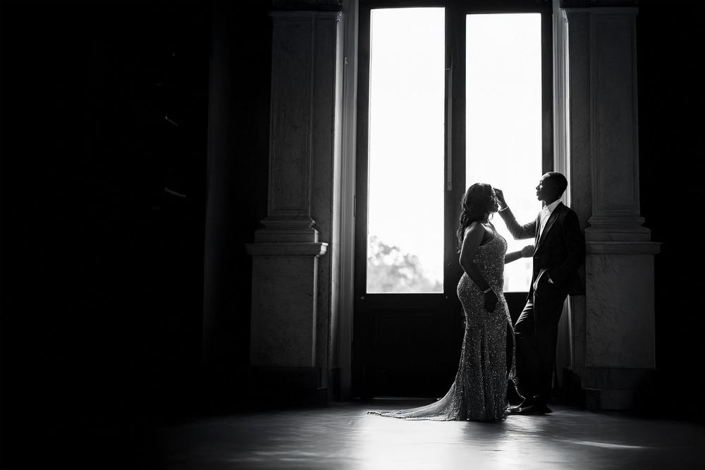Silhouettes of a couple stand in dramatic window light creating a moody artistic composition.