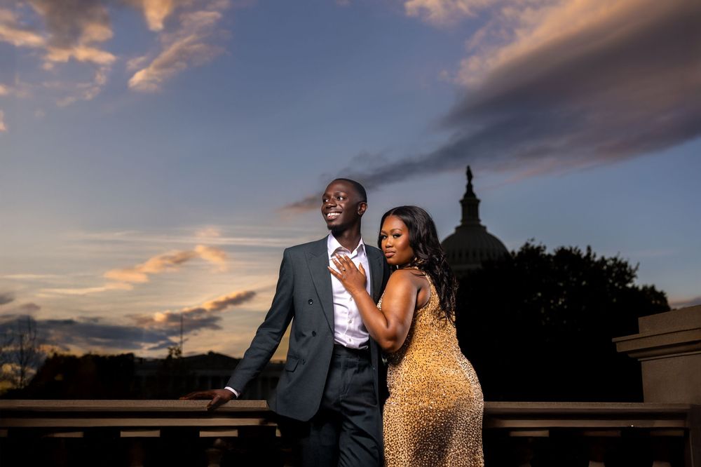 A couple embraces against a dramatic sunset sky with architectural silhouettes of DC Capitol in the background.