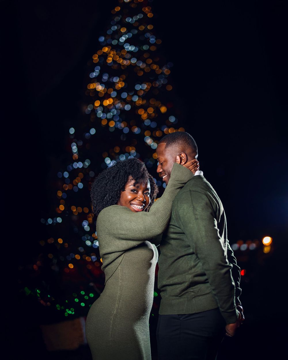 A couple embraces in an intimate moment against a backdrop of twinkling bokeh lights at night.