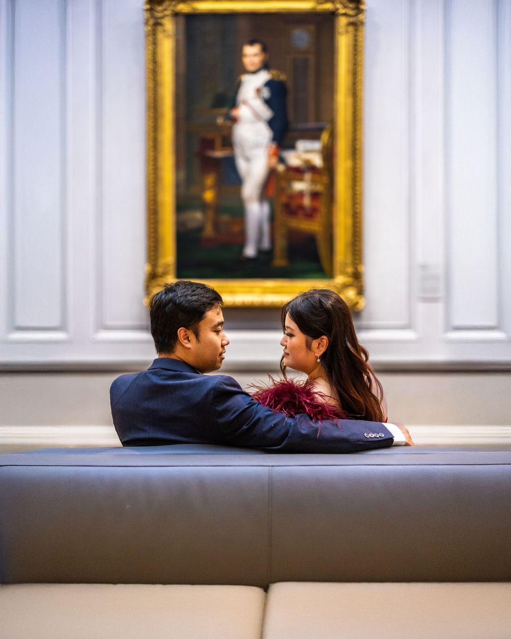 Romantic couple resting on museum bench surrounded by gold-framed artwork.