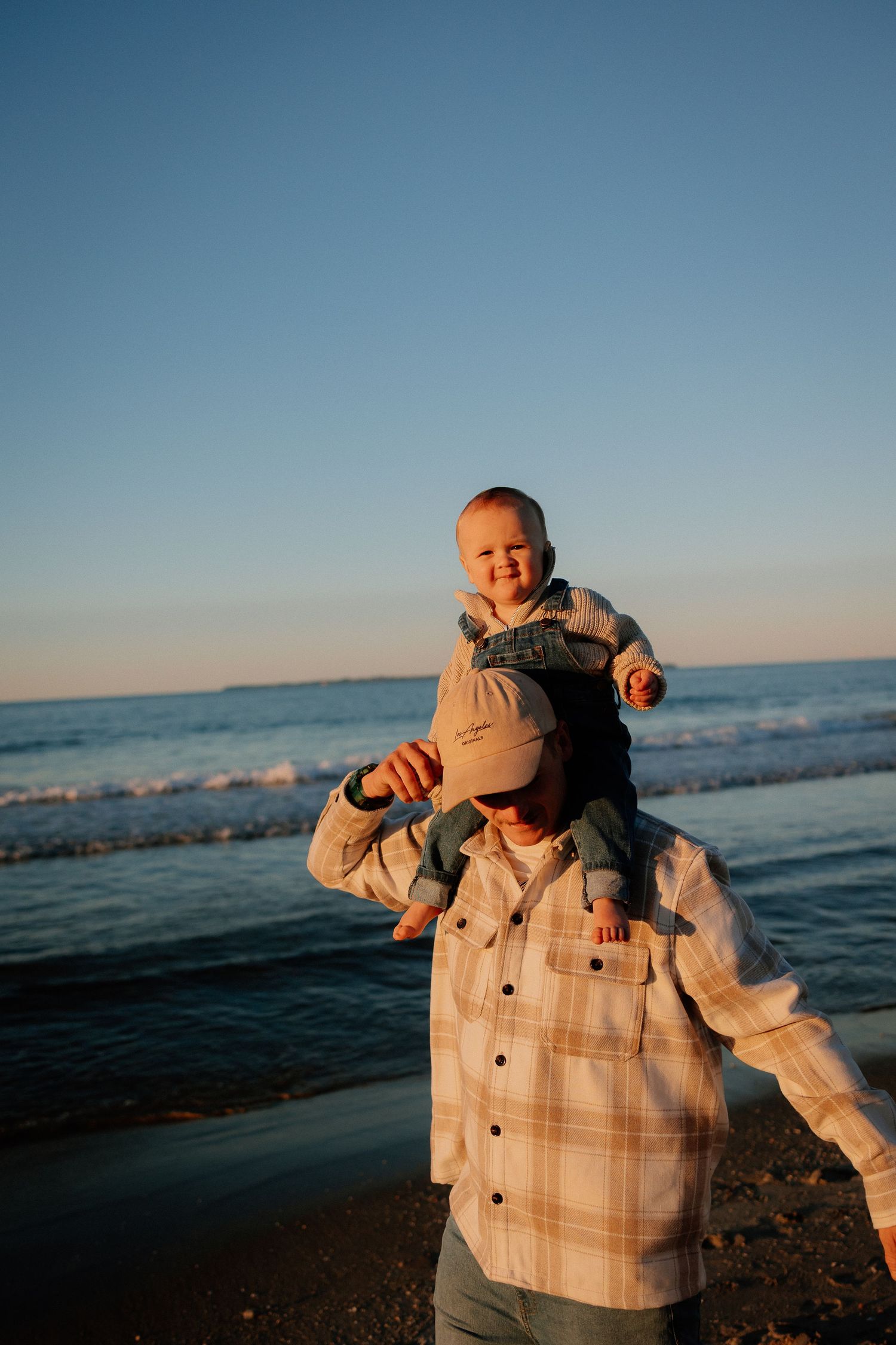 Against a blue sky background, someone tosses a small child wearing beige clothing joyfully into the air.