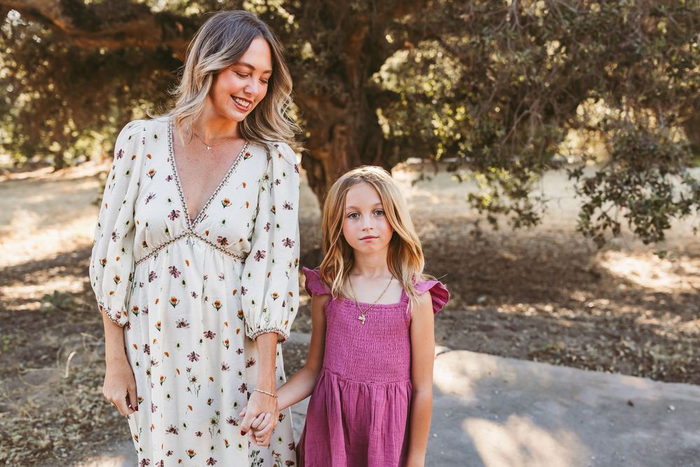 Two people wearing coordinating rust floral and magenta dresses pose together in outdoor autumn setting.
