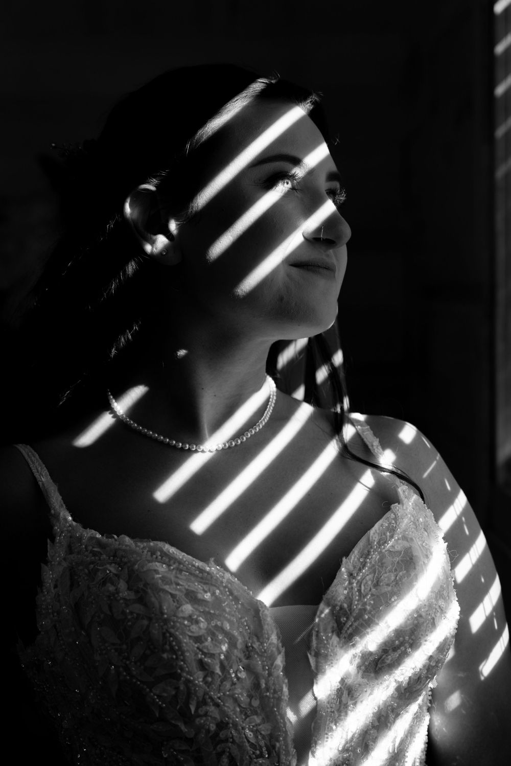 Dramatic black and white portrait with window blind shadows creating artistic lighting effects.