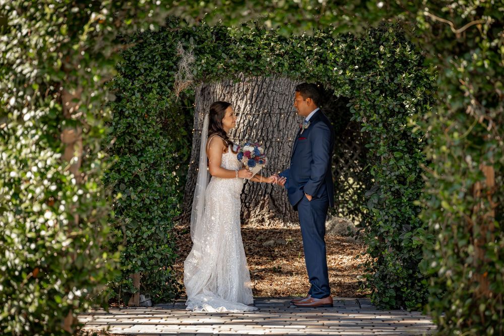 A couple shares an intimate moment under a natural green archway in an outdoor garden setting.