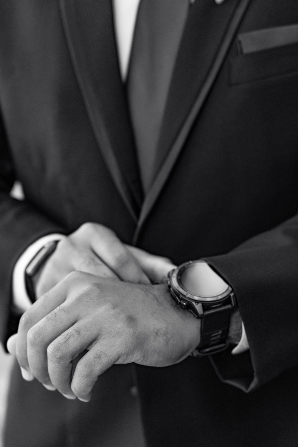 Close-up sequence of hands adjusting a black suit jacket and watch during wedding preparation.