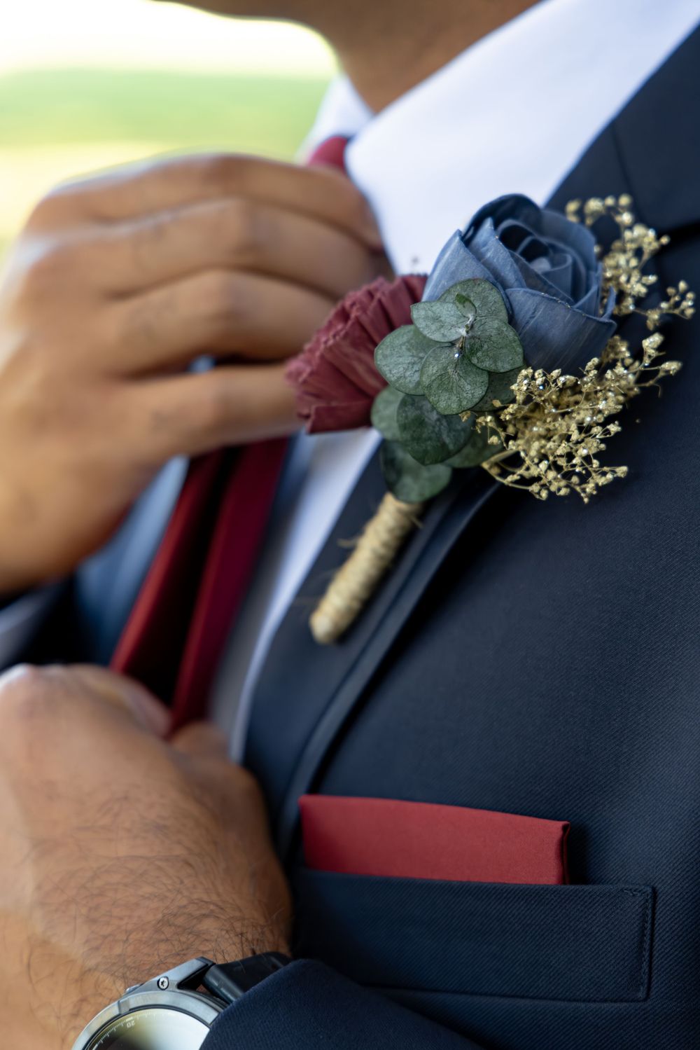 Close-up view of a burgundy boutonniere with eucalyptus leaves pinned to a navy suit jacket.
