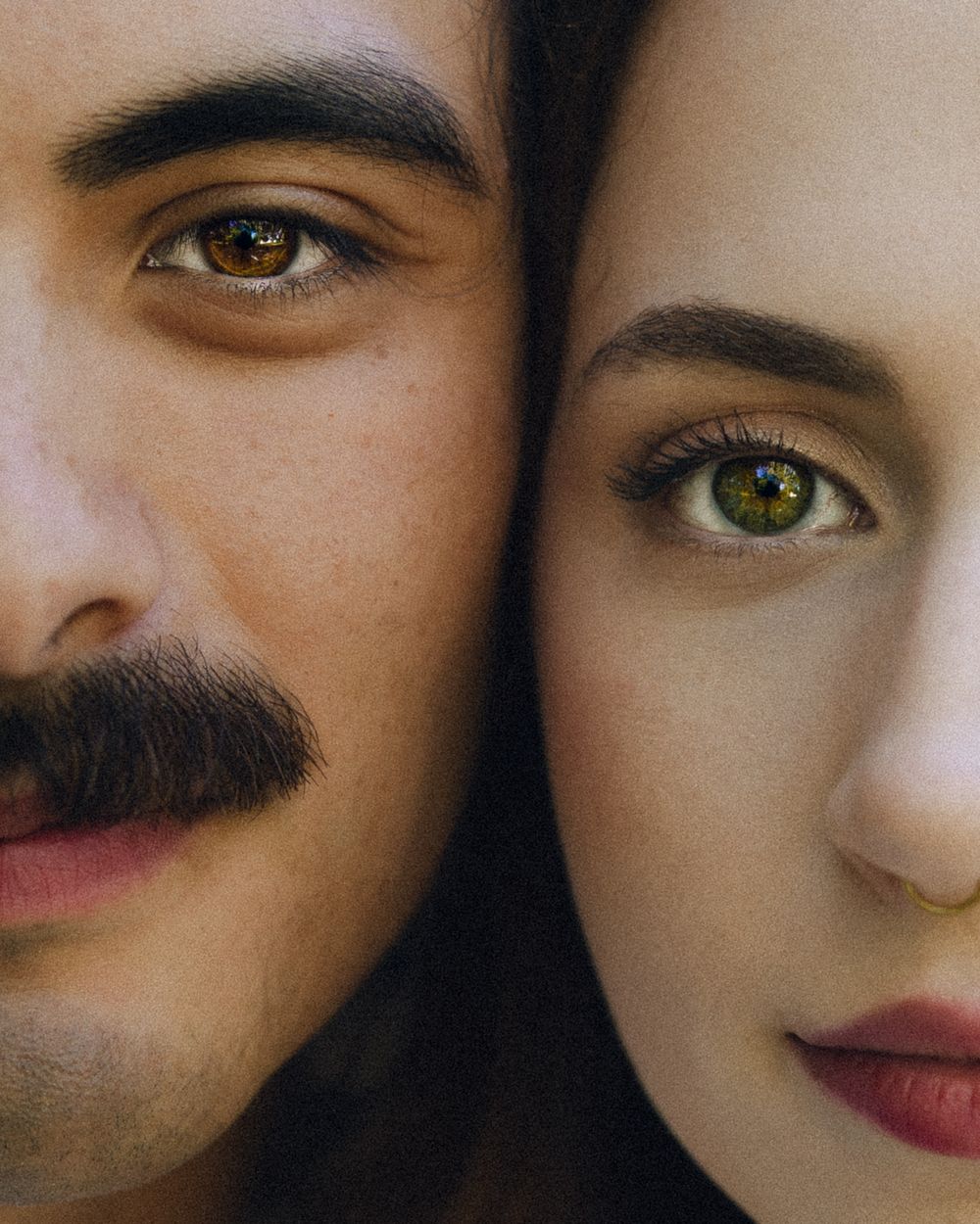 Close-up portrait of a man with mustache and a woman with green eyes, faces side by side.
