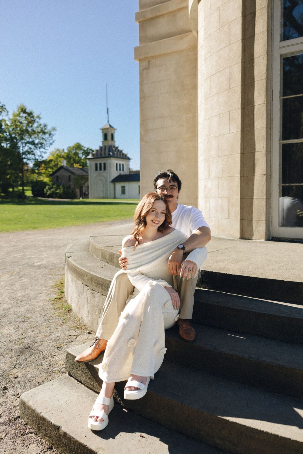 A couple sits together on stone steps of a grand building in warm sunlight, creating romantic portraits.
