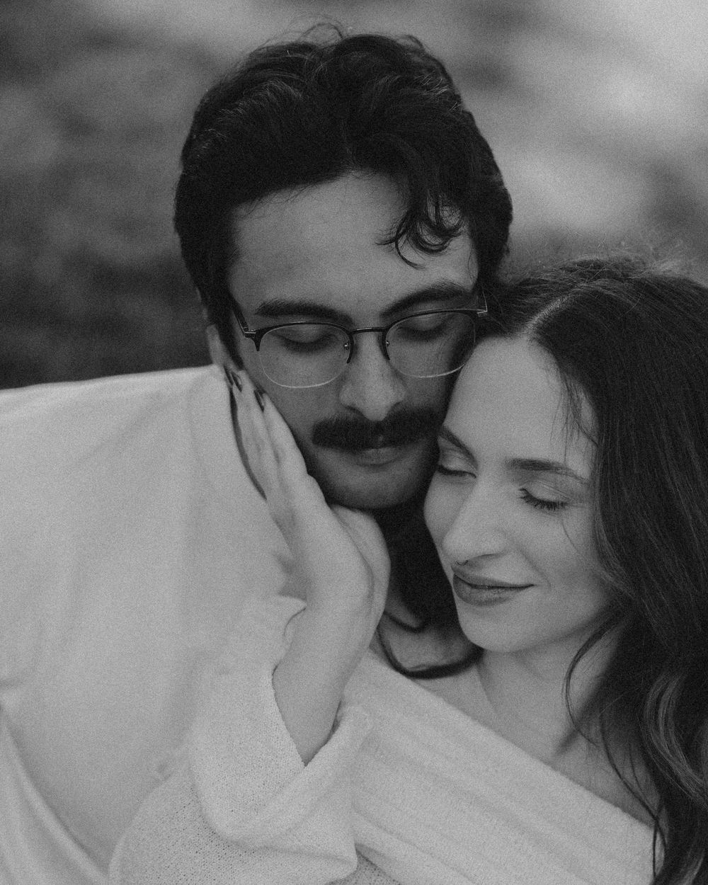 Black and white photo of a romantic couple embracing, man with glasses and mustache resting against woman's hand.