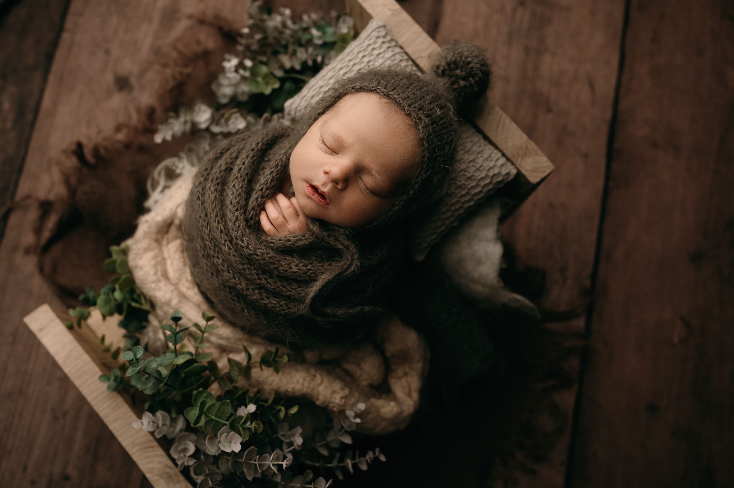 A person in a brown knit sweater lies on wooden floorboards surrounded by green ivy plants.