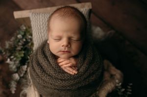 A sleeping newborn baby wrapped in a cozy brown knitted blanket during a professional photography session.