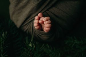 Close-up photo of tiny bare feet against a dark fabric background with green grass visible below.