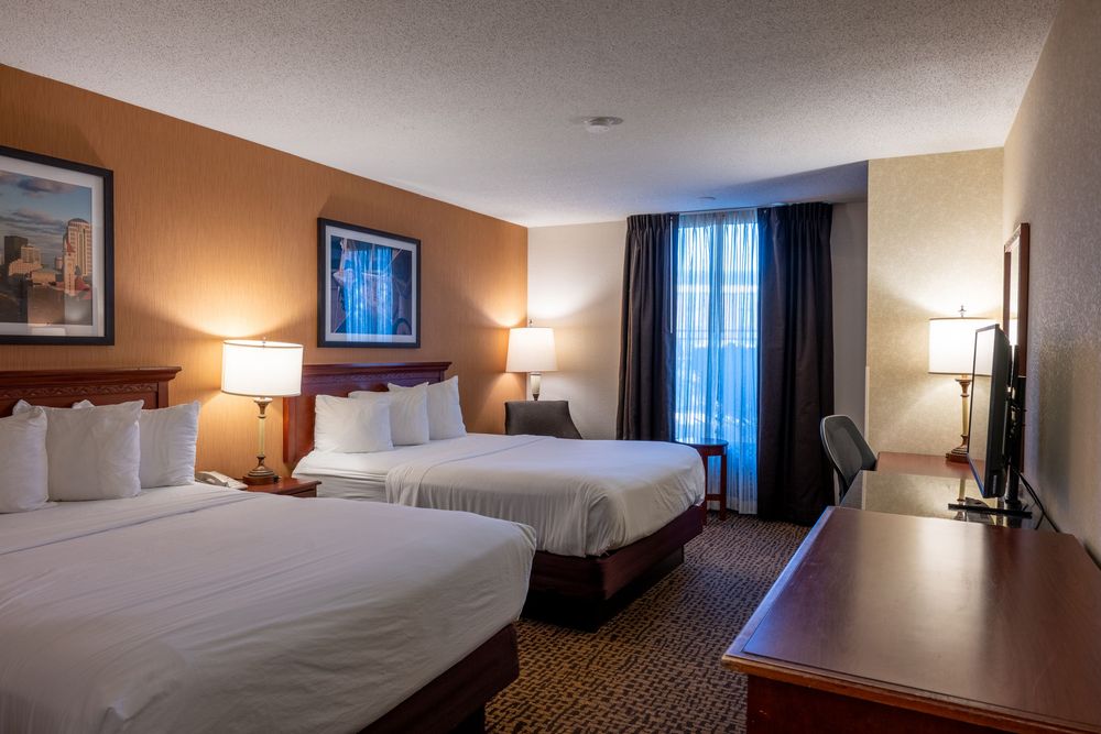 Modern hotel room interior with queen bed, desk area, and window showing warm lighting and contemporary furnishings.