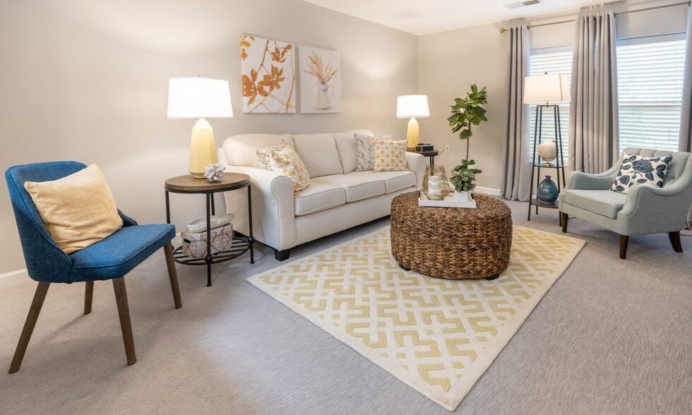 Modern living room with beige sofa, blue accent chair, geometric rug, and woven coffee table in neutral tones.