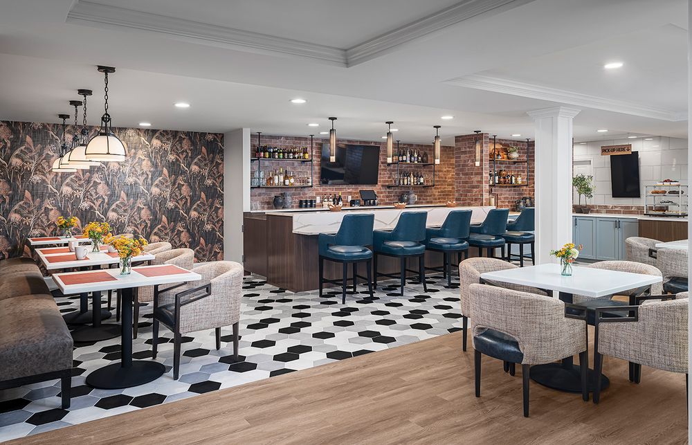 Modern restaurant interior with black and white checkered floor, blue bar stools, and floral wallpaper accent wall.