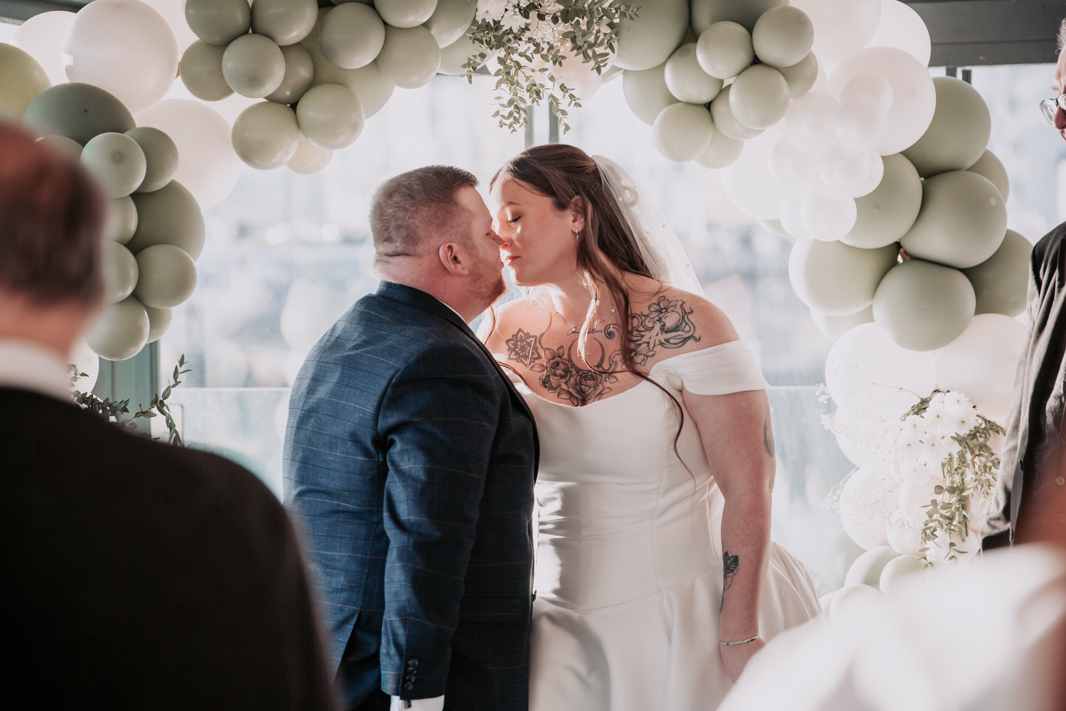 A romantic wedding couple shares intimate moments under a beautiful white balloon arch and floral decorations.