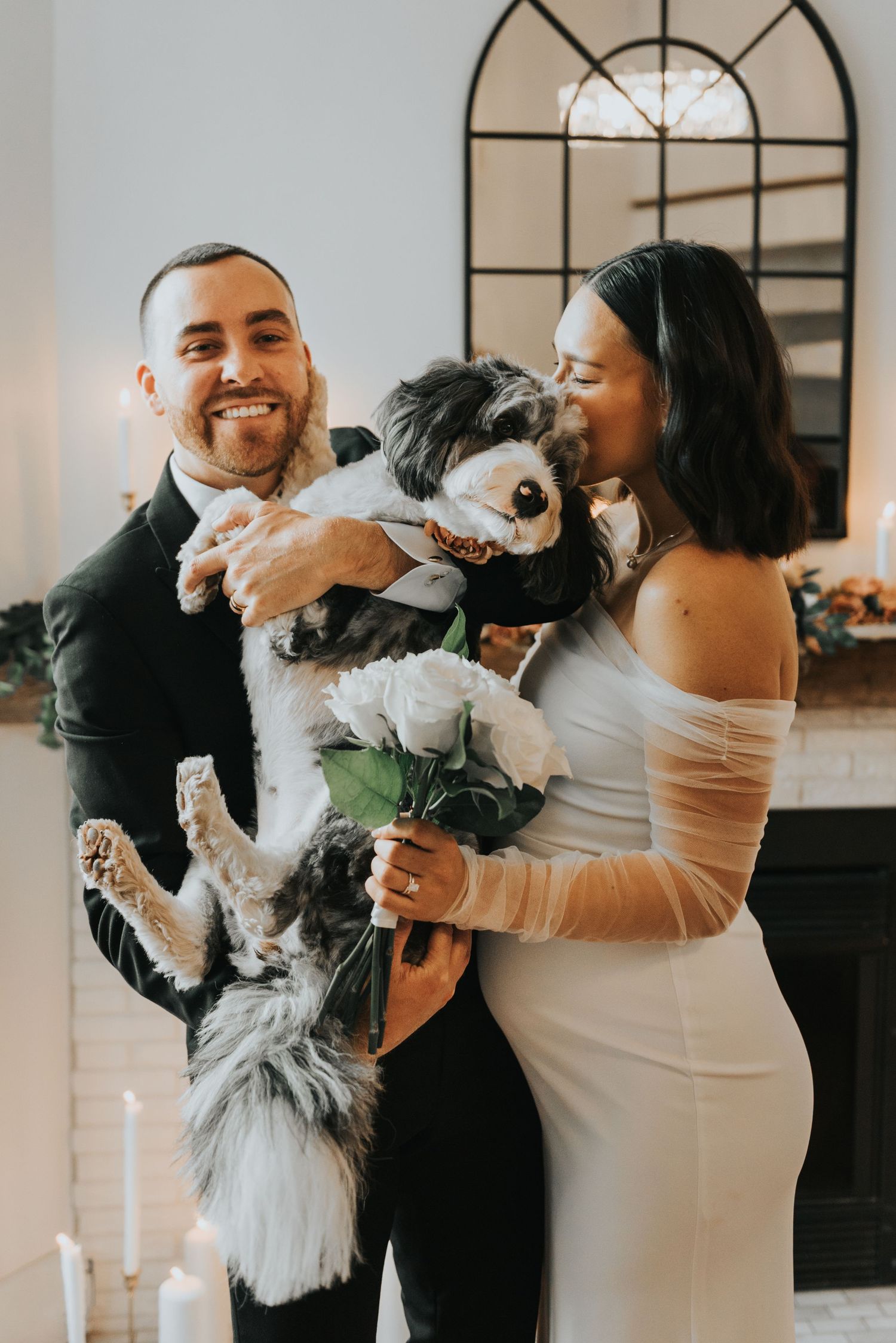 A couple plays with their small black and white dog in a bright indoor setting.