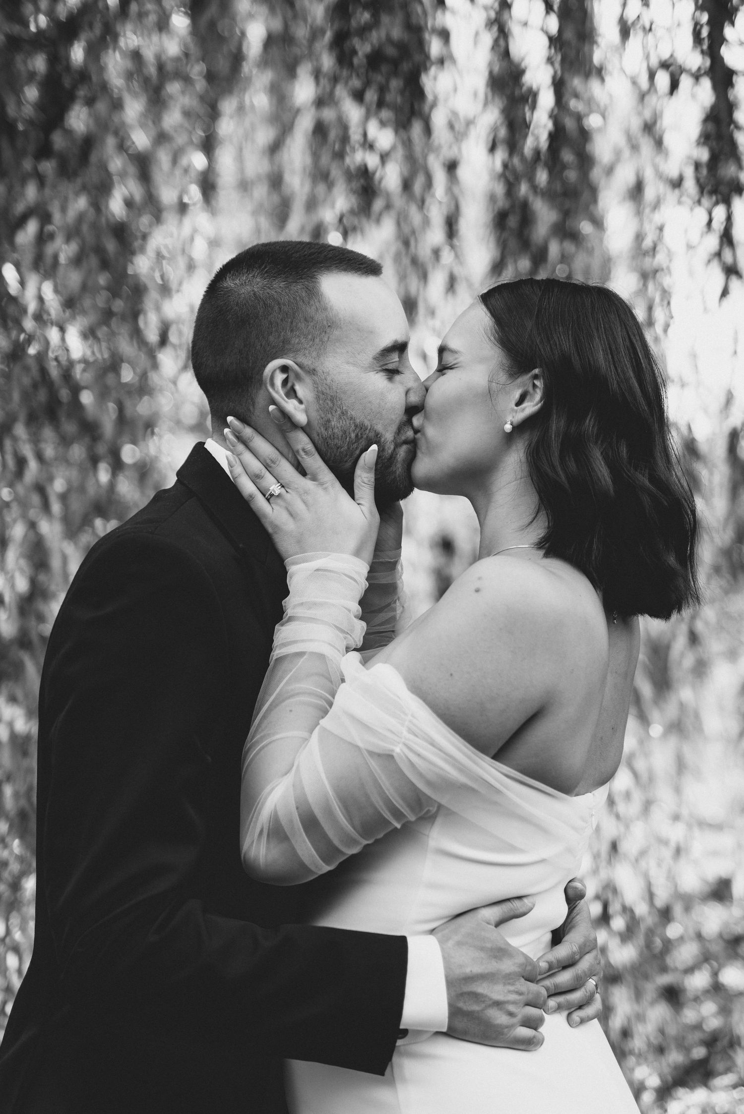 A romantic couple shares intimate kisses against a backdrop of hanging willow branches.