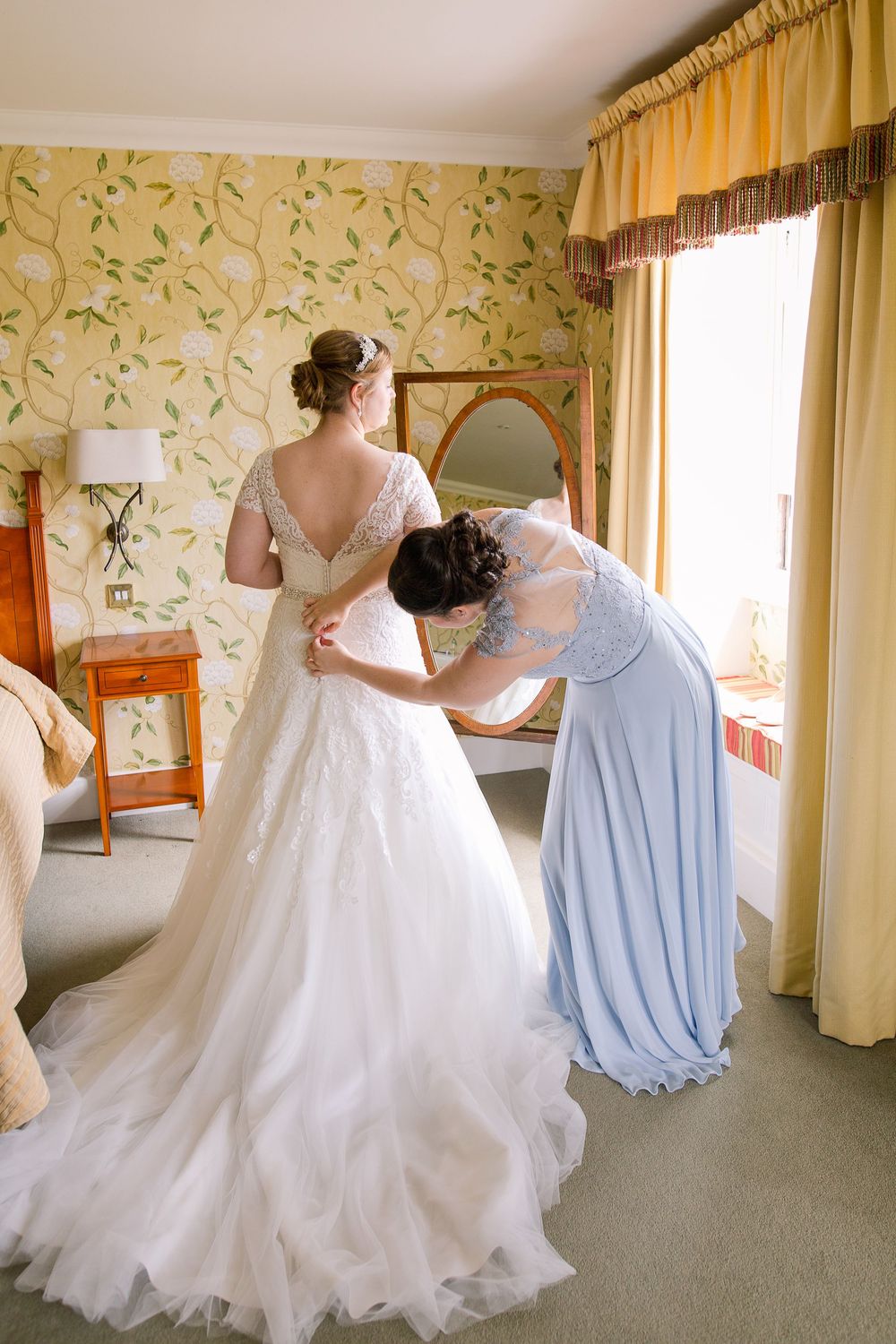 A wedding dress with flowing tulle skirt is shown in multiple angles as it moves gracefully in a room with floral wallpaper.