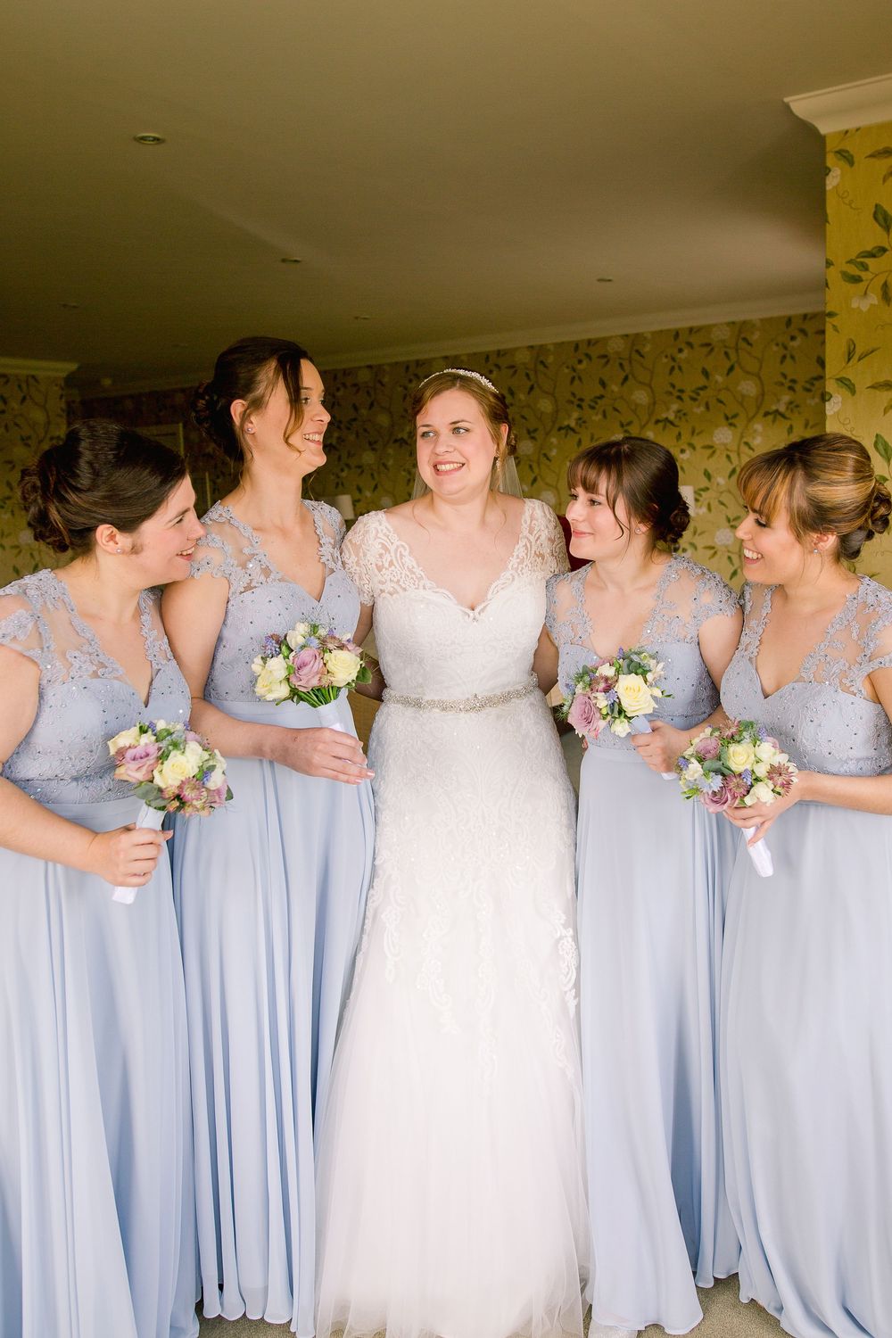 Bridesmaids in flowing light blue dresses stand in a row with bouquets during a wedding celebration.