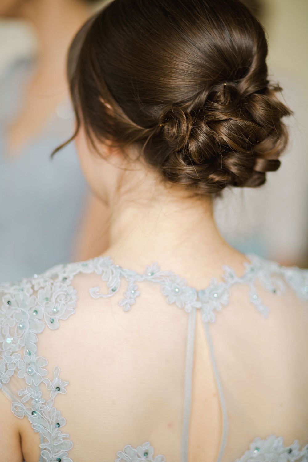 Elegant bridal updo hairstyle with intricate braiding shown from behind with delicate light blue beaded lace dress detail.