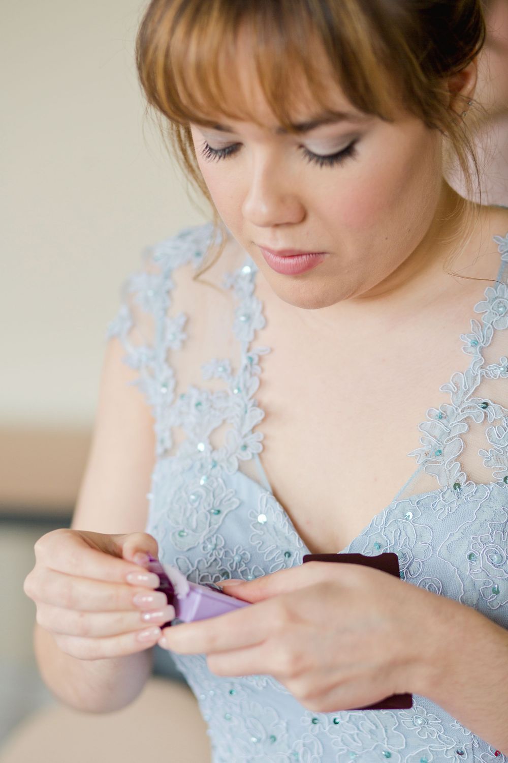 Woman in light blue lace dress delicately fastens jewelry while getting ready.