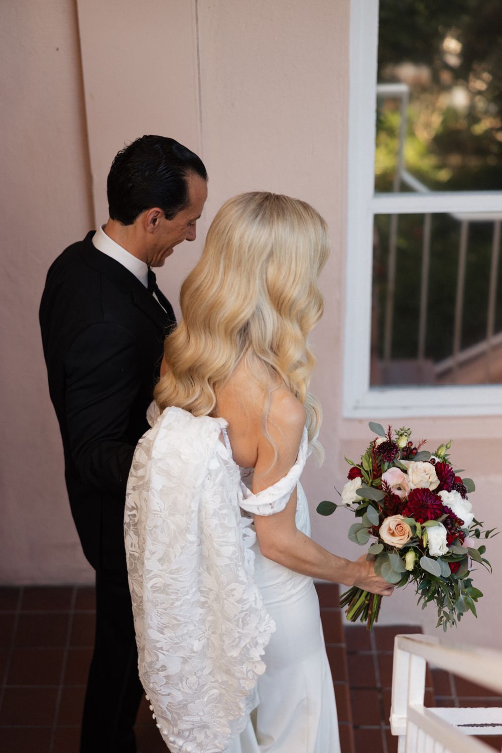 A couple shares an intimate first look moment before their wedding ceremony, with the bride holding a burgundy bouquet.