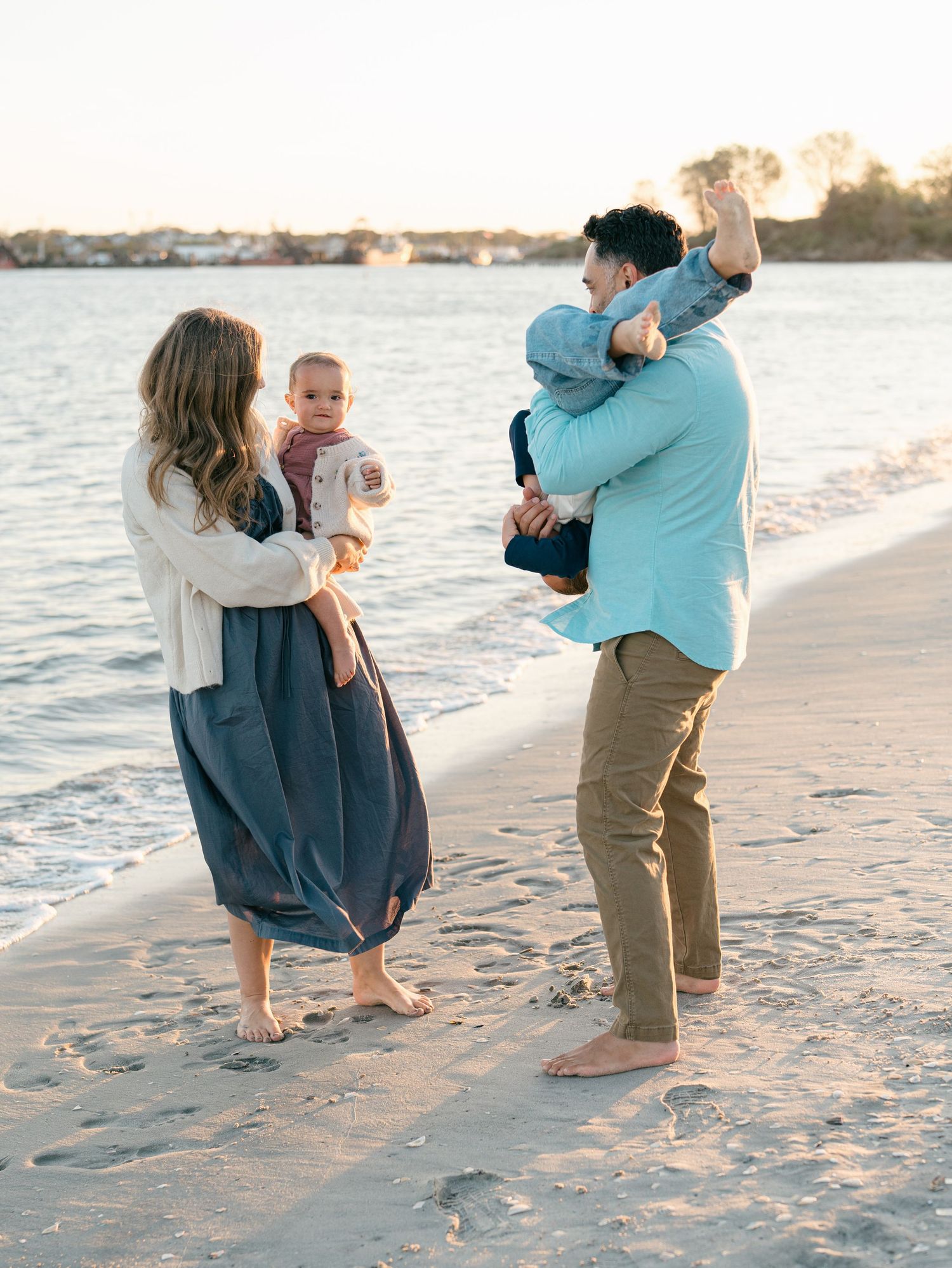 A father flips his son upside down while smiling at his wife who is holding their baby girl.