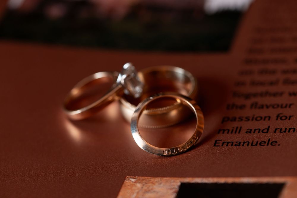 Wedding rings and engagement rings are arranged artistically on a brown surface in warm lighting.