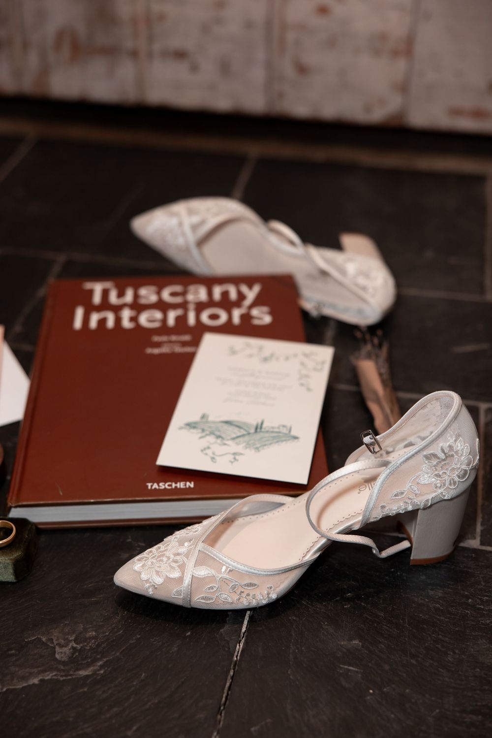 White ballet shoes and brown Tuscany books arranged artistically on a dark surface in moody lighting.