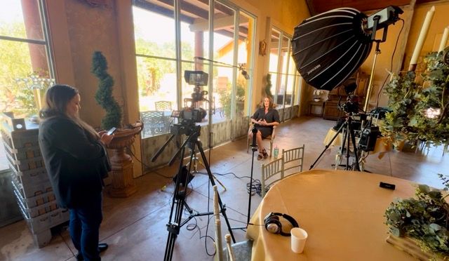 Behind-the-scenes video production setup with camera equipment and lighting in a bright indoor space.