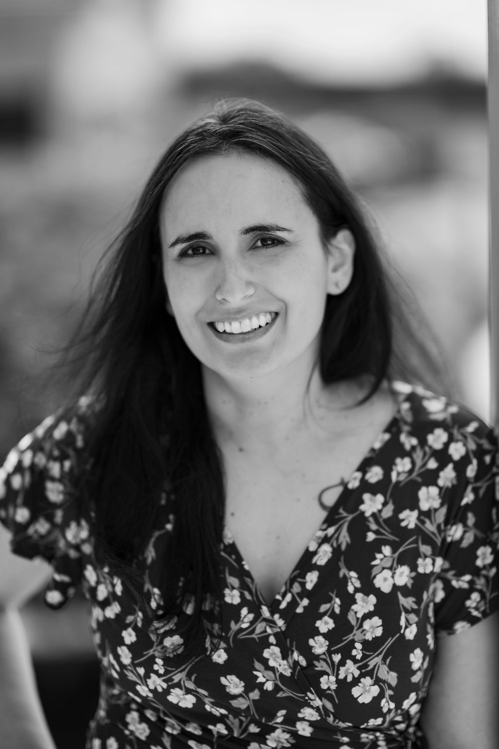 Smiling young woman with long dark hair wearing floral dress in black and white portrait.