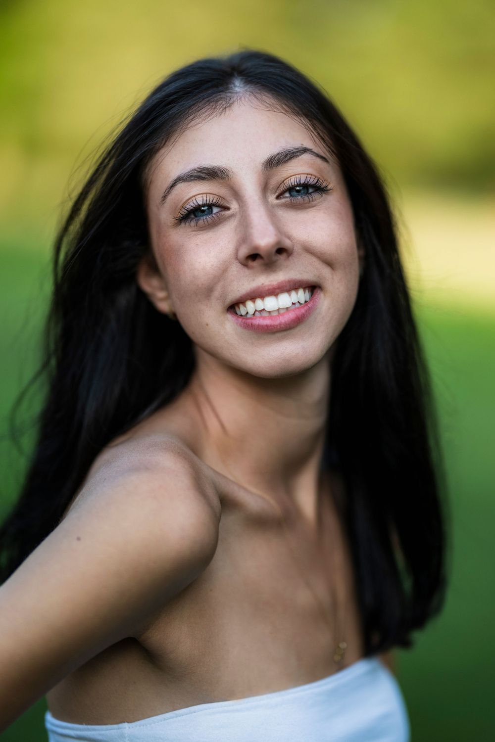 Young woman with long dark hair smiling outdoors against green background.