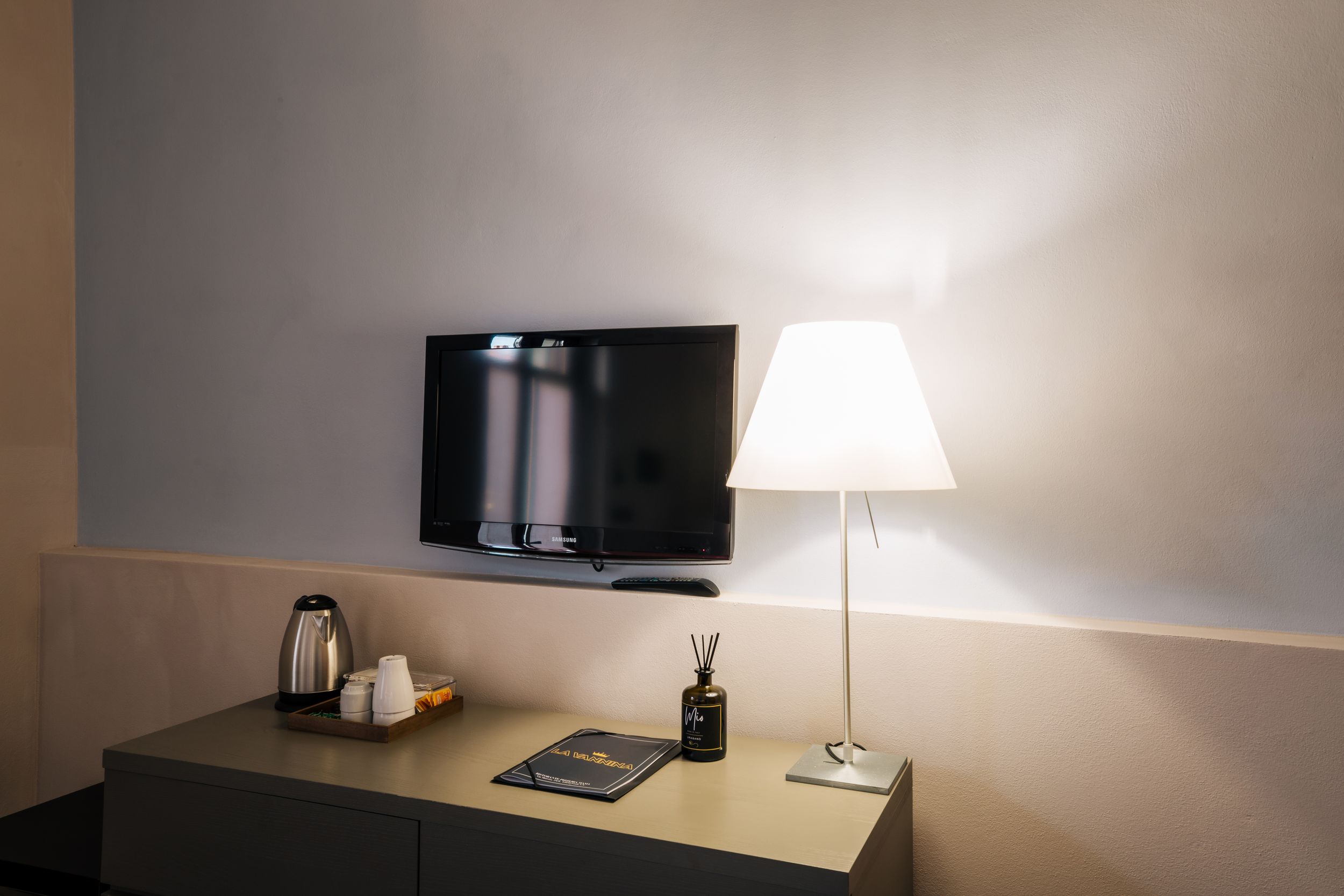 Minimalist home office desk setup with lamp, tablet, and diffuser against beige wall in warm lighting.