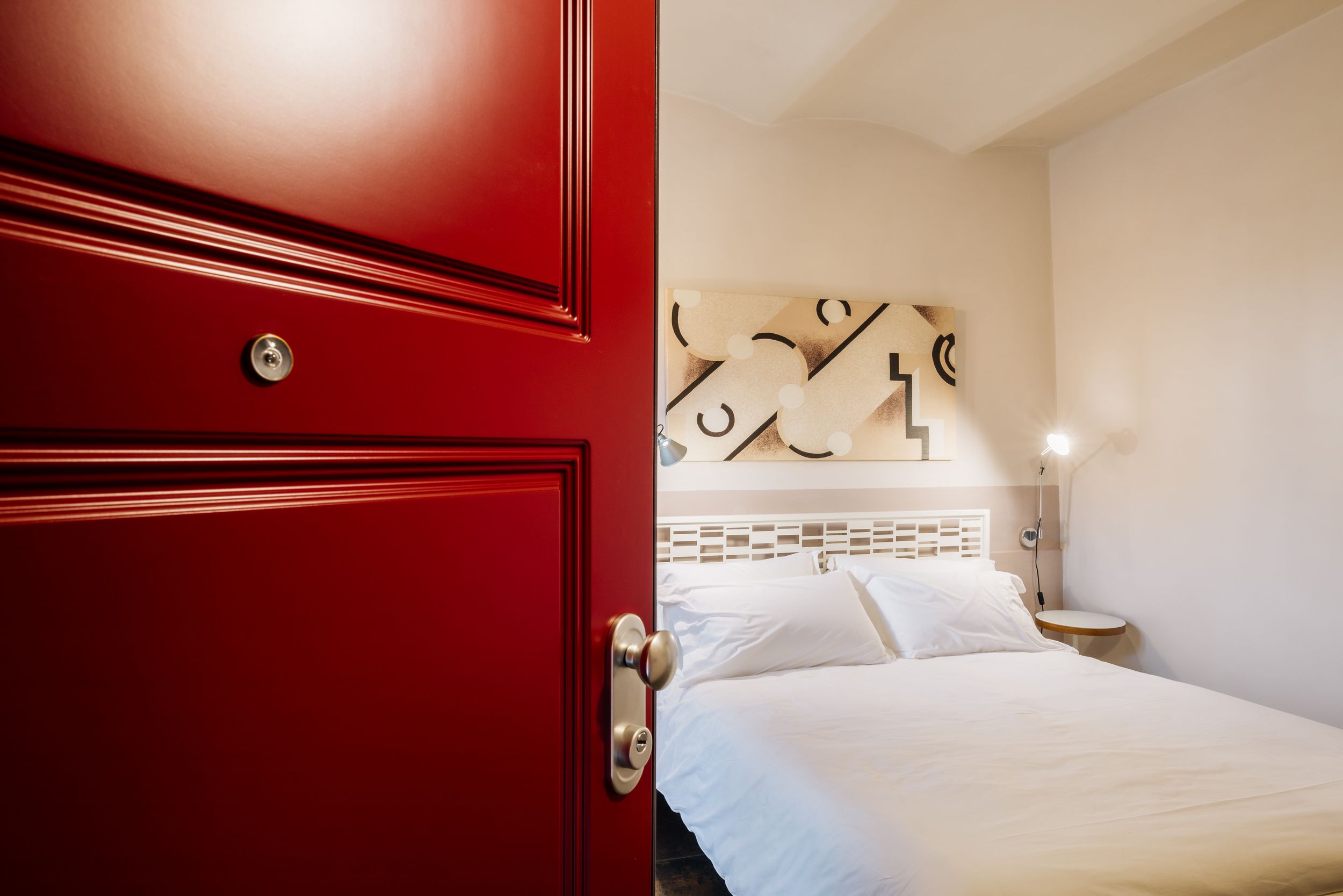 Modern hotel room interior with red accent door and white bedding in warm neutral tones.
