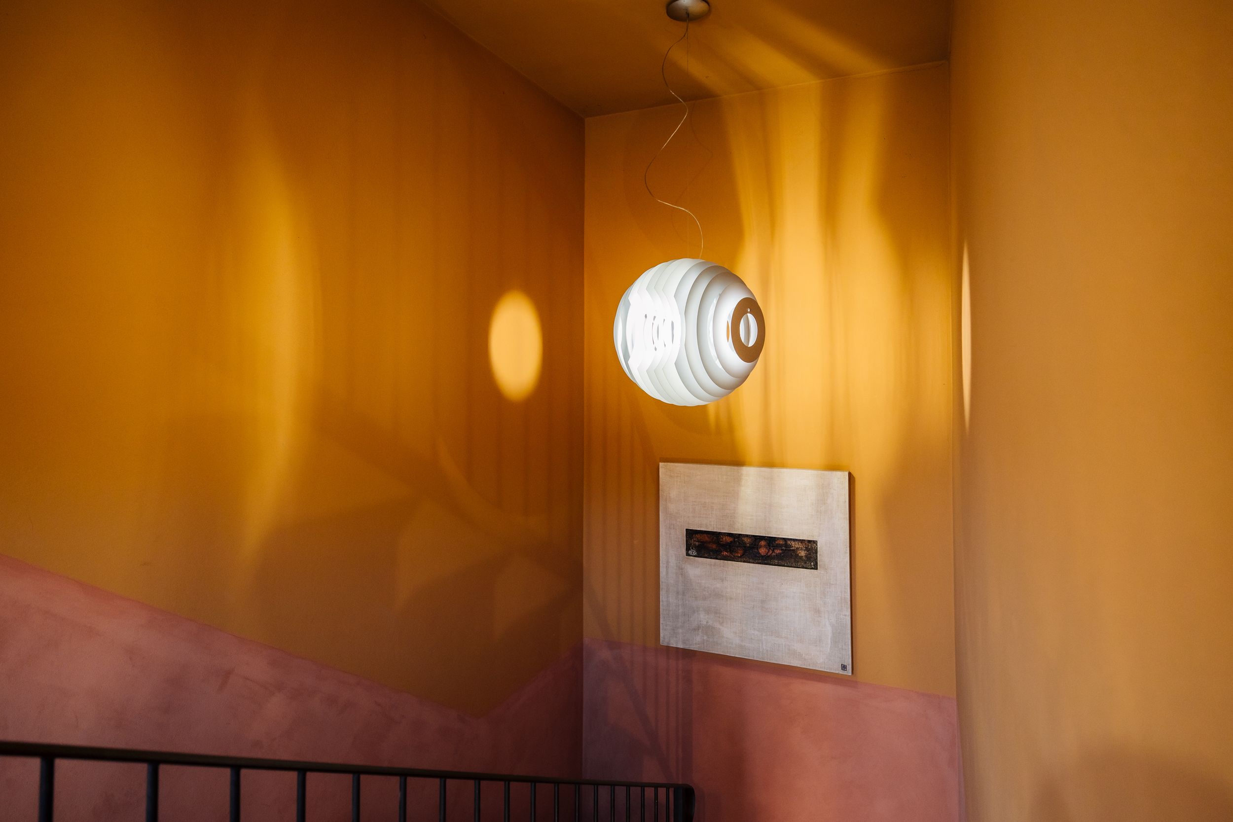 Round white ceiling light fixture mounted on orange-tinted wall creates warm ambient lighting in hallway.